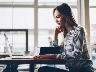 A woman dressed in business casual sitting at a table and working on SEO related things with her laptop.